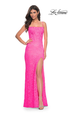 A woman models the Neon Pink Long Lace Prom Dress: La Femme 32423, featuring spaghetti straps, a sheer corset bodice, and a high side slit. She poses with one hand on her hip. The La Femme logo appears in the top right corner.