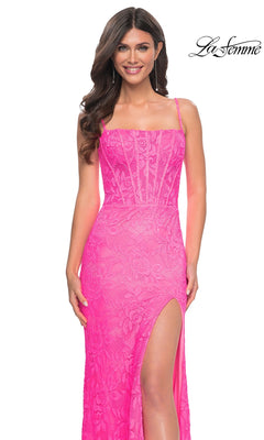 A woman models the Neon Pink Long Lace Prom Dress: La Femme 32423, featuring thin straps, a thigh-high slit, and a sheer corset-style bodice. The "La Femme" logo appears in the top right corner.