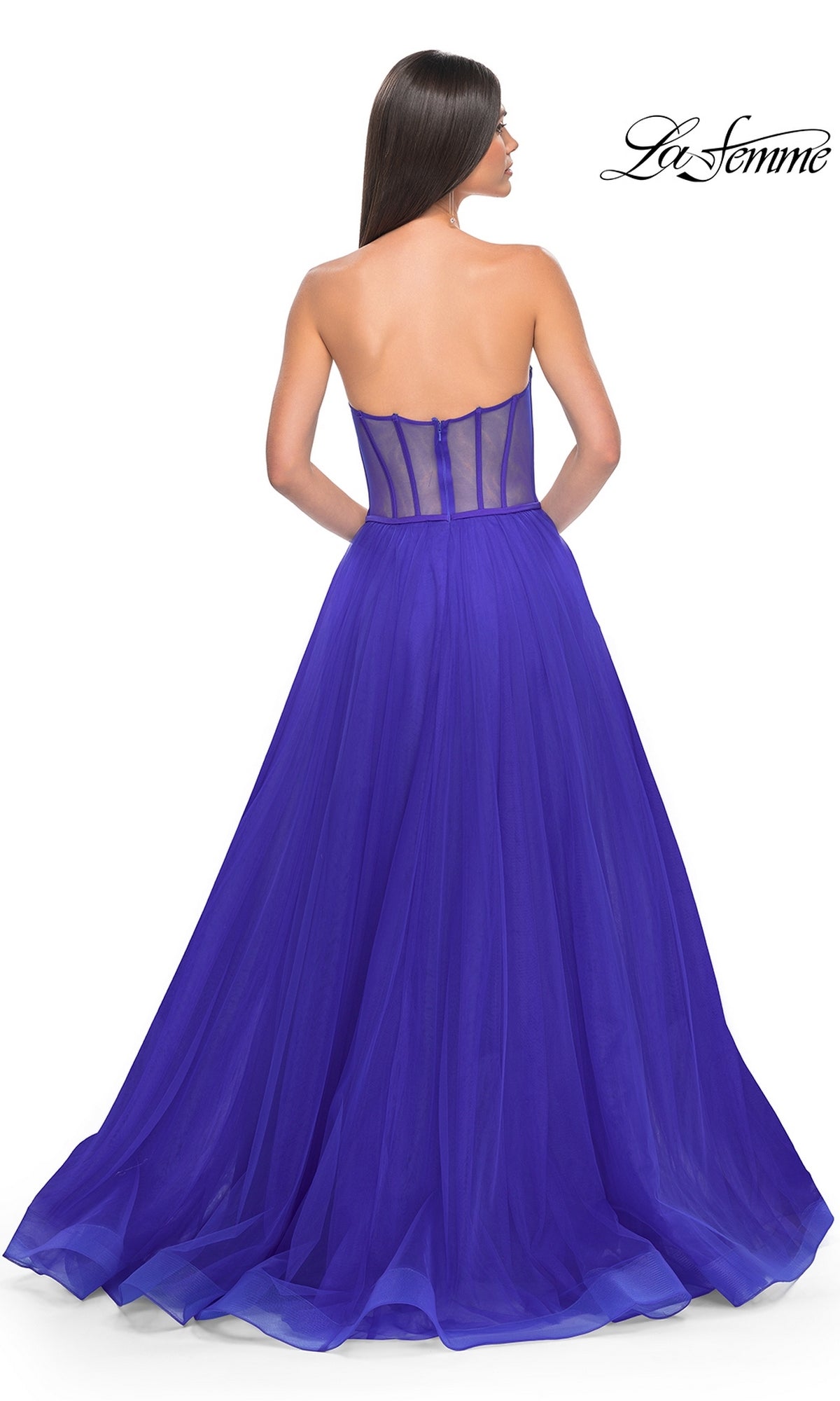 A woman stands with her back to the camera in the La Femme 32424, a royal blue, strapless long tulle prom dress featuring a corset-style bodice and sheer back.