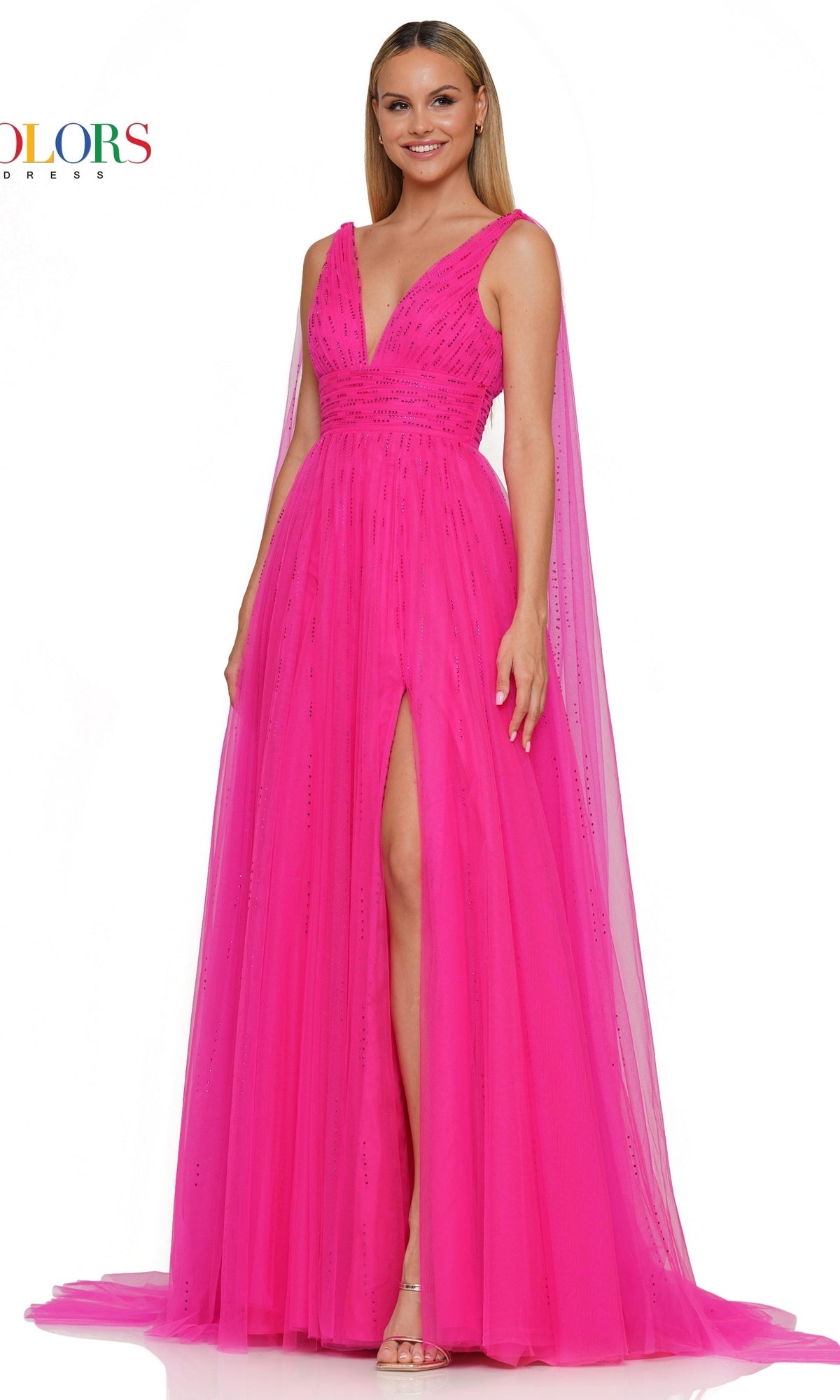 A woman wears the Colors Dress 3242, a Classic Long Prom Ball Gown in hot pink with a v-neck, sleeveless design, floor-length sheer tulle, deep front slit, and cape-like shoulder extensions.