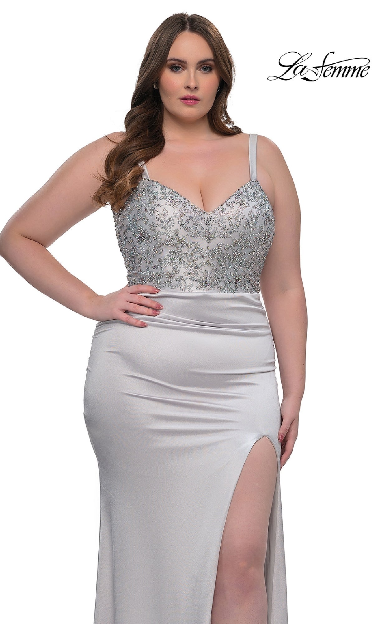A woman models the La Femme 32430, a plus-size long satin prom dress featuring a rhinestone-beaded bodice and thigh-high slit, standing before a white background with the 
