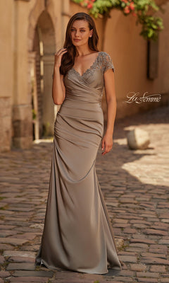 A woman stands on a cobblestone street wearing the La Femme 32431, a pewter long formal dress with a floor-length V-neck and beaded shoulder embellishments.