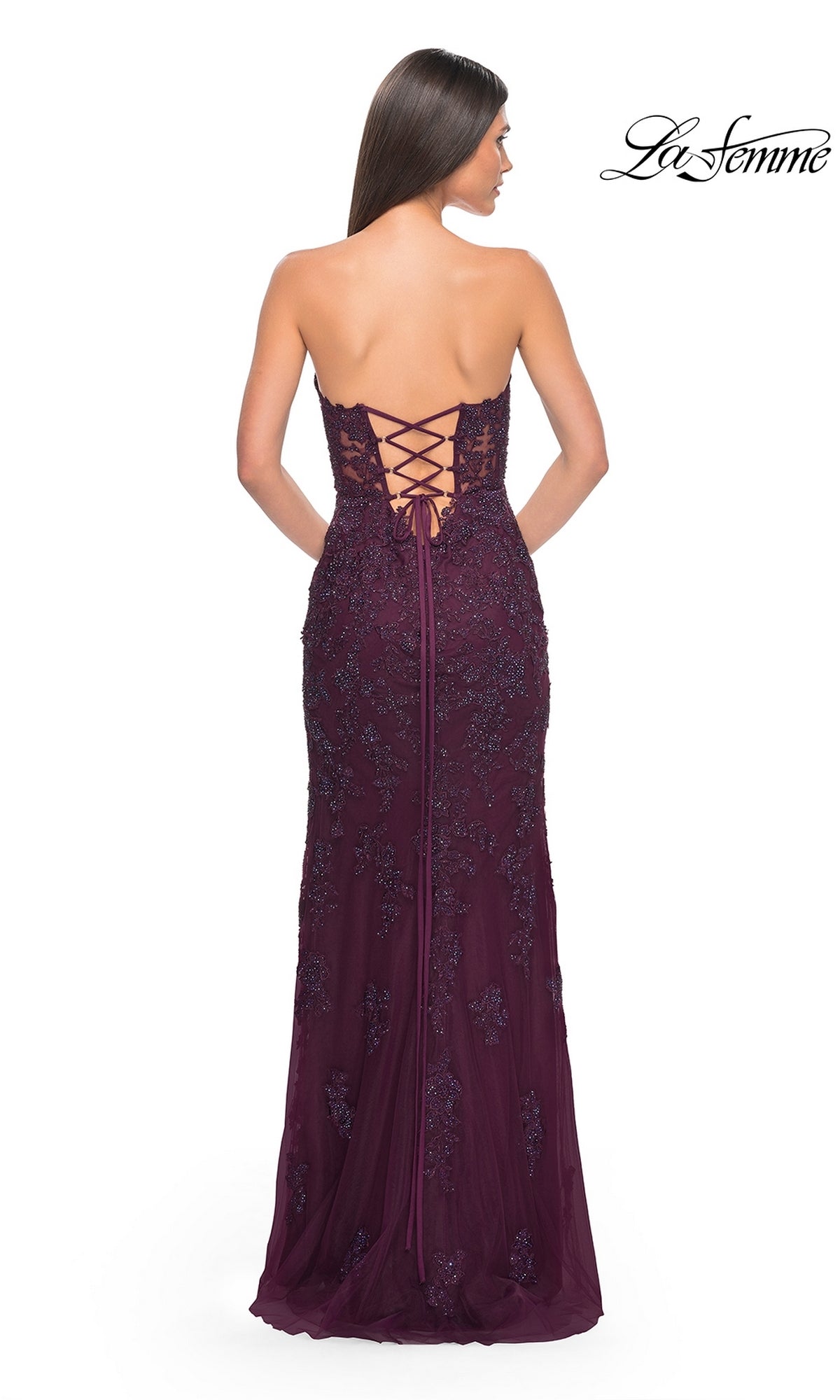 A woman in the La Femme 32437 beaded-lace long prom dress, a strapless dark purple gown with a sweetheart neckline, lace-up back, and sequin details, stands facing away from the camera.