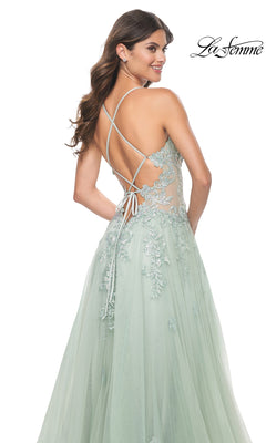 A woman poses and smiles over her shoulder in the Sheer-Waist Long A-Line Prom Dress: La Femme 32438, featuring light green color, embroidered lace appliqué details, and an open crisscross back.