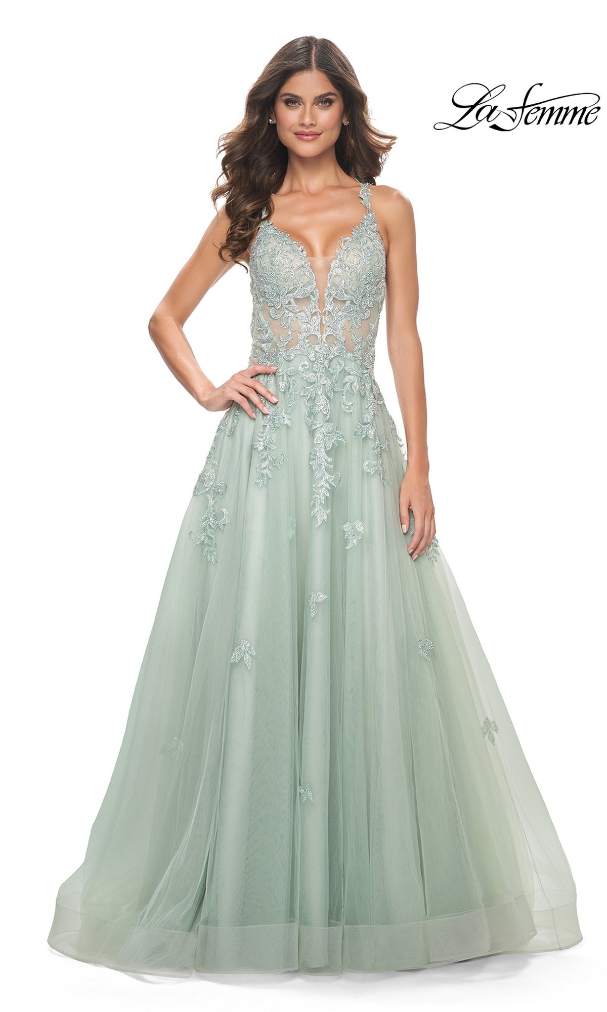 A woman in the Sheer-Waist Long A-Line Prom Dress (La Femme 32438), featuring light green floral lace, a sheer bodice, and sleeveless design, stands against a white background with the 