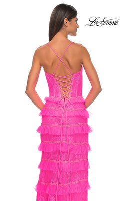 Woman poses with her back to the camera in the Ruffled Long Beaded-Lace Prom Dress, La Femme 32442—a bright pink gown with a crisscross lace-up back and intricate lace detailing. "La Femme" logo appears in the top right corner.