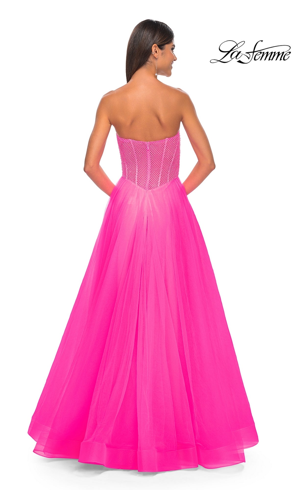 A woman faces away, wearing the La Femme 32445: a bright pink strapless long A-line prom dress with a corset-style embellished bodice and flowing tulle skirt. The 