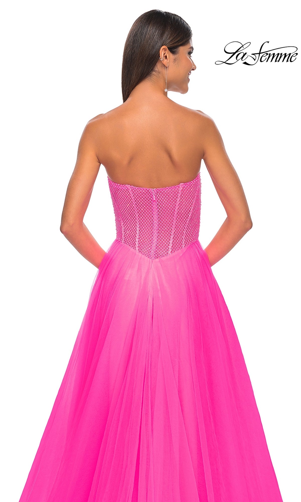 Woman wears the La Femme 32445 Strapless Long A-Line Prom Dress—bright pink with a fitted corset bodice, mesh details, and a flowing skirt—shown from the back against a white background.