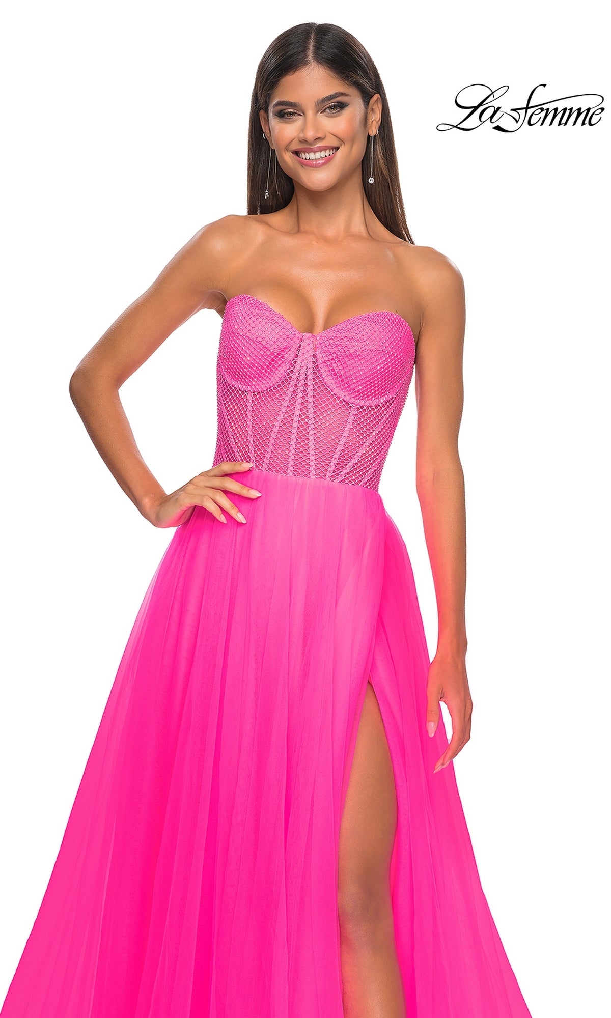 A woman poses and smiles in the La Femme 32445 Strapless Long A-Line Prom Dress, featuring a bright pink corset-style bodice, sheer detailing, and a thigh-high slit.