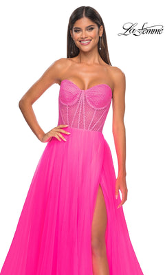 A woman poses and smiles in the La Femme 32445 Strapless Long A-Line Prom Dress, featuring a bright pink corset-style bodice, sheer detailing, and a thigh-high slit.