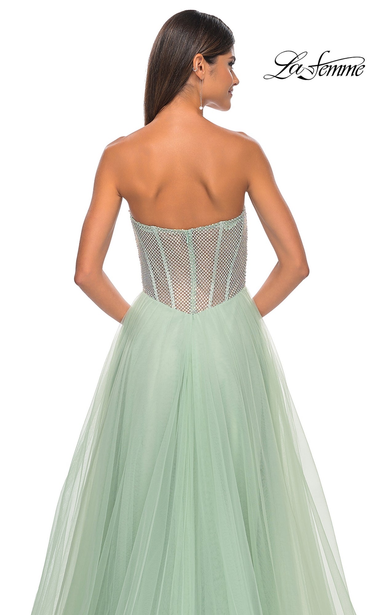 A woman faces away, showcasing the La Femme 32445 strapless long A-line prom dress in pale green with a sheer corset bodice and flowing tulle skirt. The 