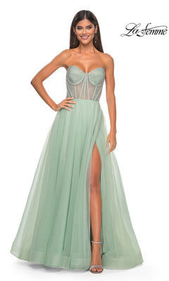 A woman stands and smiles against a white background, wearing the La Femme 32445 strapless long A-line prom dress in light green, which features a sheer corset-style bodice and a thigh-high slit.
