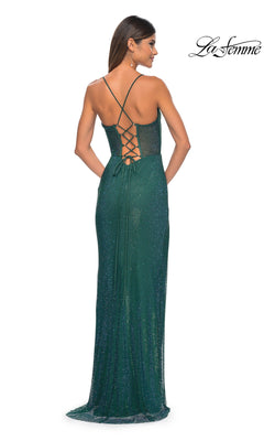 A woman stands facing away, wearing the Sheer-Bodice Long La Femme Fishnet Prom Gown 32446 in green, featuring sparkly fishnet fabric, a corset-style bodice, thin crisscross straps, and a lace-up back.