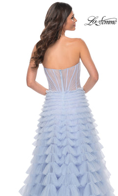 A woman models the Long Ruffled A-Line Prom Ball Gown: La Femme 32447, featuring a strapless light blue tiered tulle skirt and fitted sheer corset bodice, shown from the back with the "La Femme" logo at top right.