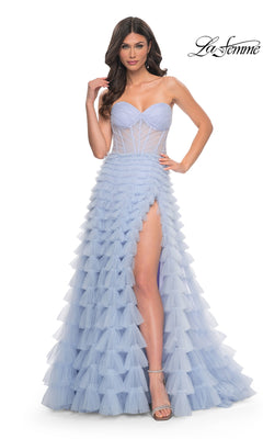 A woman wears the La Femme 32447: a strapless light blue long ruffled A-line prom ball gown with a sheer corset bodice, tiered skirt, and high slit, paired with strappy heels. The La Femme logo appears in the corner.
