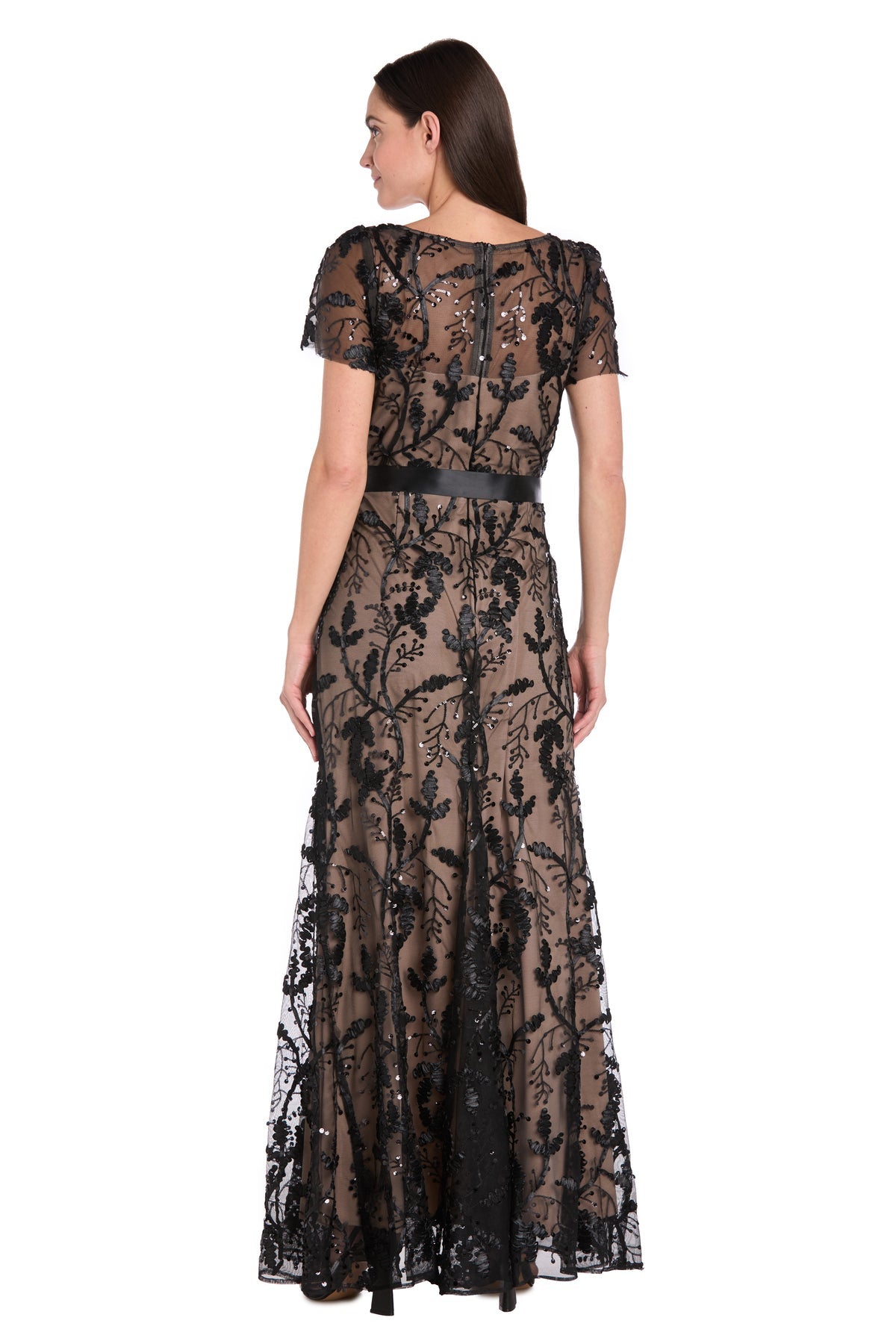 A woman is seen from the back wearing the R&M Richards 3253 Short Sleeve Black Formal Dress, a floor-length lace gown with floral patterns.