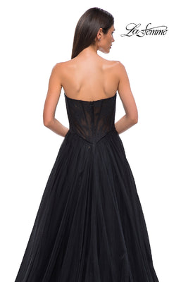 A woman with long brown hair wears the La Femme 32579 strapless long prom ball gown, featuring a floral corset bodice and sheer lace back, as she stands with her back to the camera.