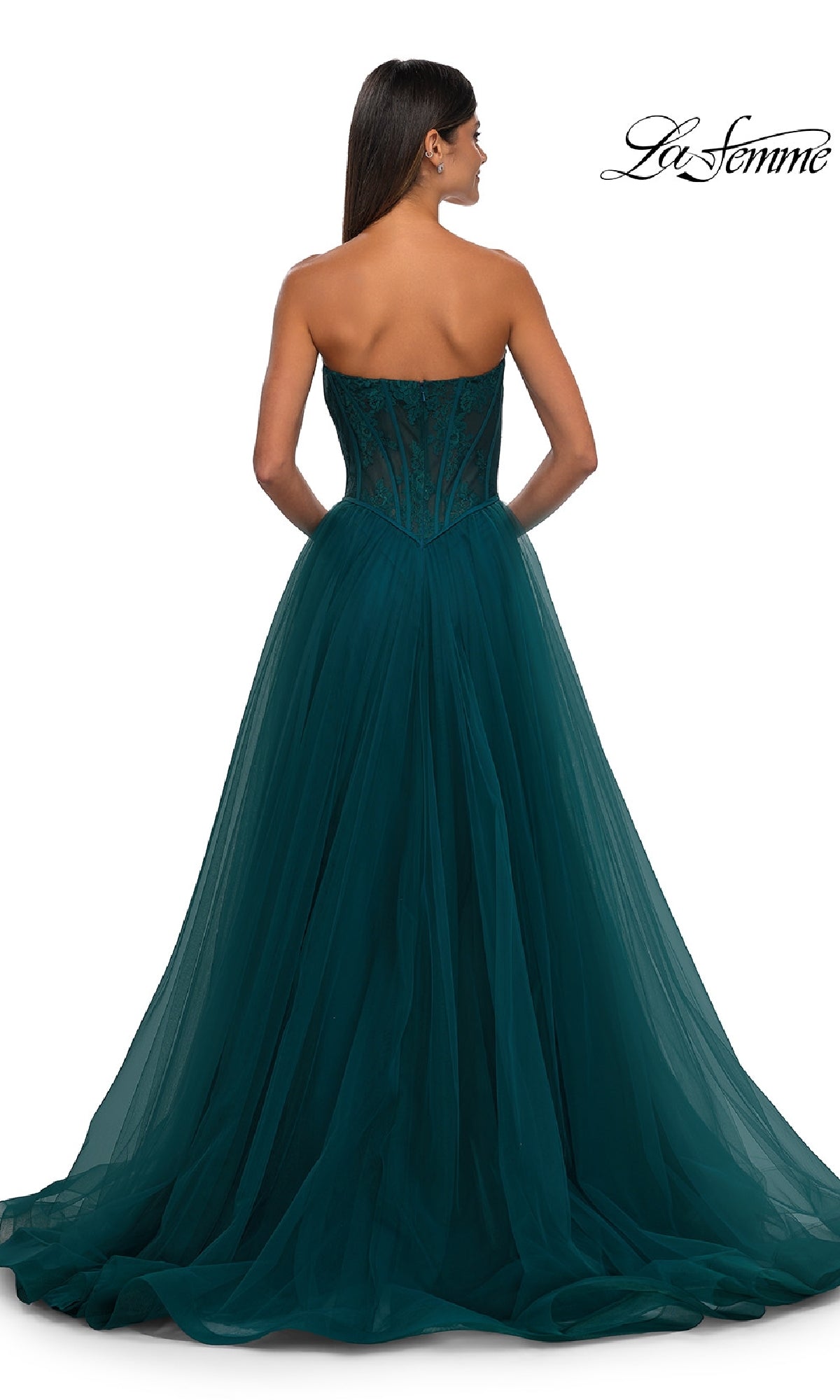 A woman elegantly models the La Femme 32579 Strapless Long Prom Ball Gown, featuring a floral corset bodice and flowing dark teal tulle skirt, shown gracefully from the back.