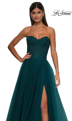A woman poses against a white background with the "La Femme" logo, wearing the Strapless Long Prom Ball Gown: La Femme 32579—featuring a sweetheart neckline, floral corset bodice, dark green lace and tulle skirt, and a high slit.