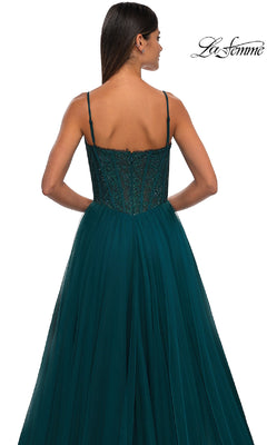 Woman in a dark teal, floor-length La Femme 32594 prom ball gown with thin straps and beaded bodice, featuring a lace corset back, standing with her back to the camera.