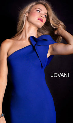 A person poses against a black background in the Jovani 32602 One-Shoulder Mermaid Prom Gown, featuring a striking blue hue and large bow detail. The brand name "JOVANI" stands out beside this stunning formal evening dress.