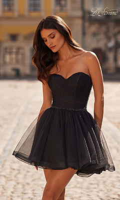 A woman poses outdoors on a cobblestone street in the La Femme Short Babydoll Tulle Homecoming Dress 32629, featuring a strapless sweetheart neckline, fitted bodice, and flared tulle skirt.