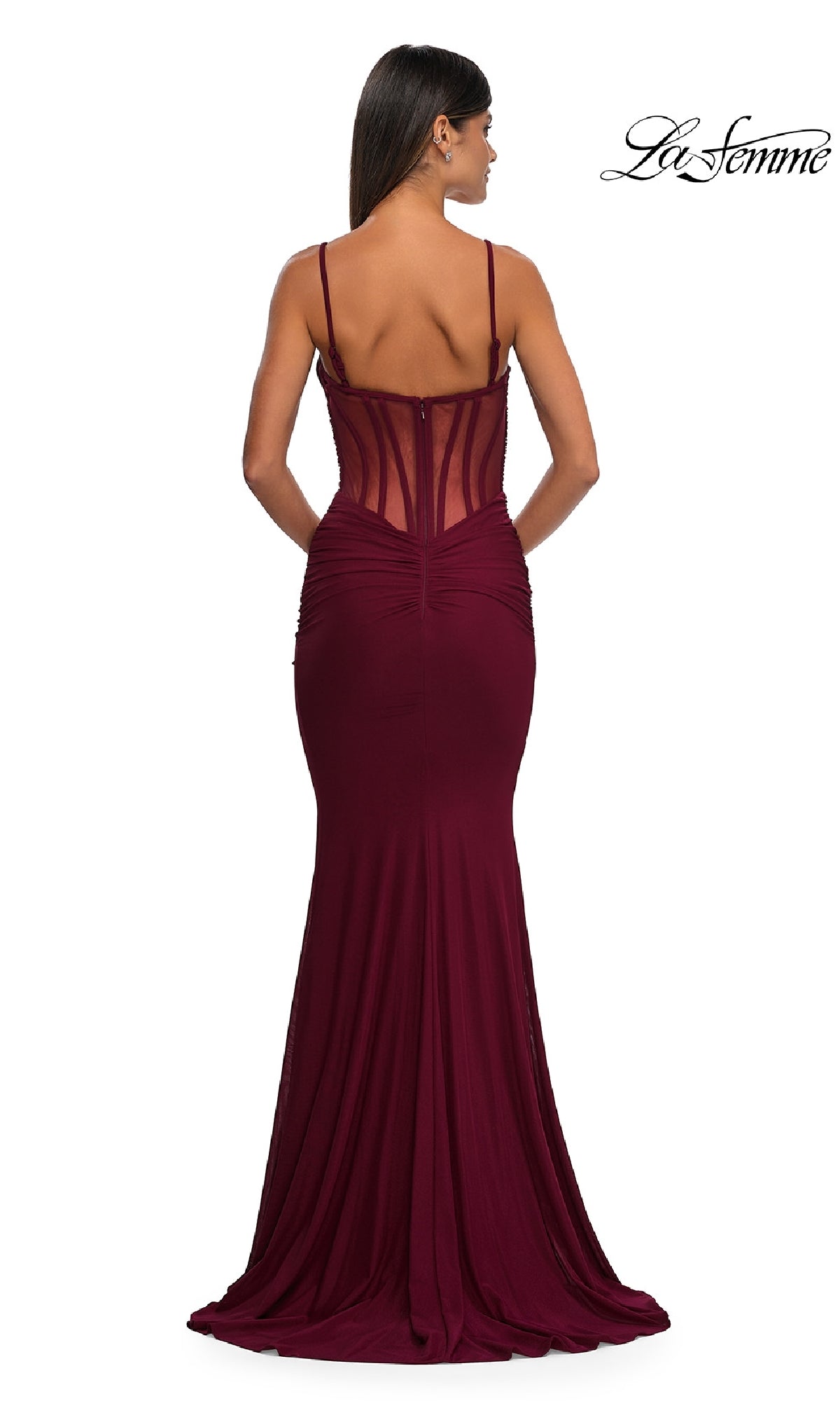 A woman faces away, wearing the fitted Sheer Low V-Neck Long Prom Dress: La Femme 32642 in maroon, which has a sheer corset bodice with thin straps. The 