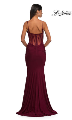 A woman faces away, wearing the fitted Sheer Low V-Neck Long Prom Dress: La Femme 32642 in maroon, which has a sheer corset bodice with thin straps. The "La Femme" logo appears in the upper right corner.