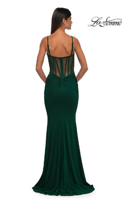 A woman in a fitted dark green Sheer Low V-Neck Long Prom Dress: La Femme 32642 with a sheer corset bodice and spaghetti straps stands with her back to the camera. La Femme logo appears in the top right corner.