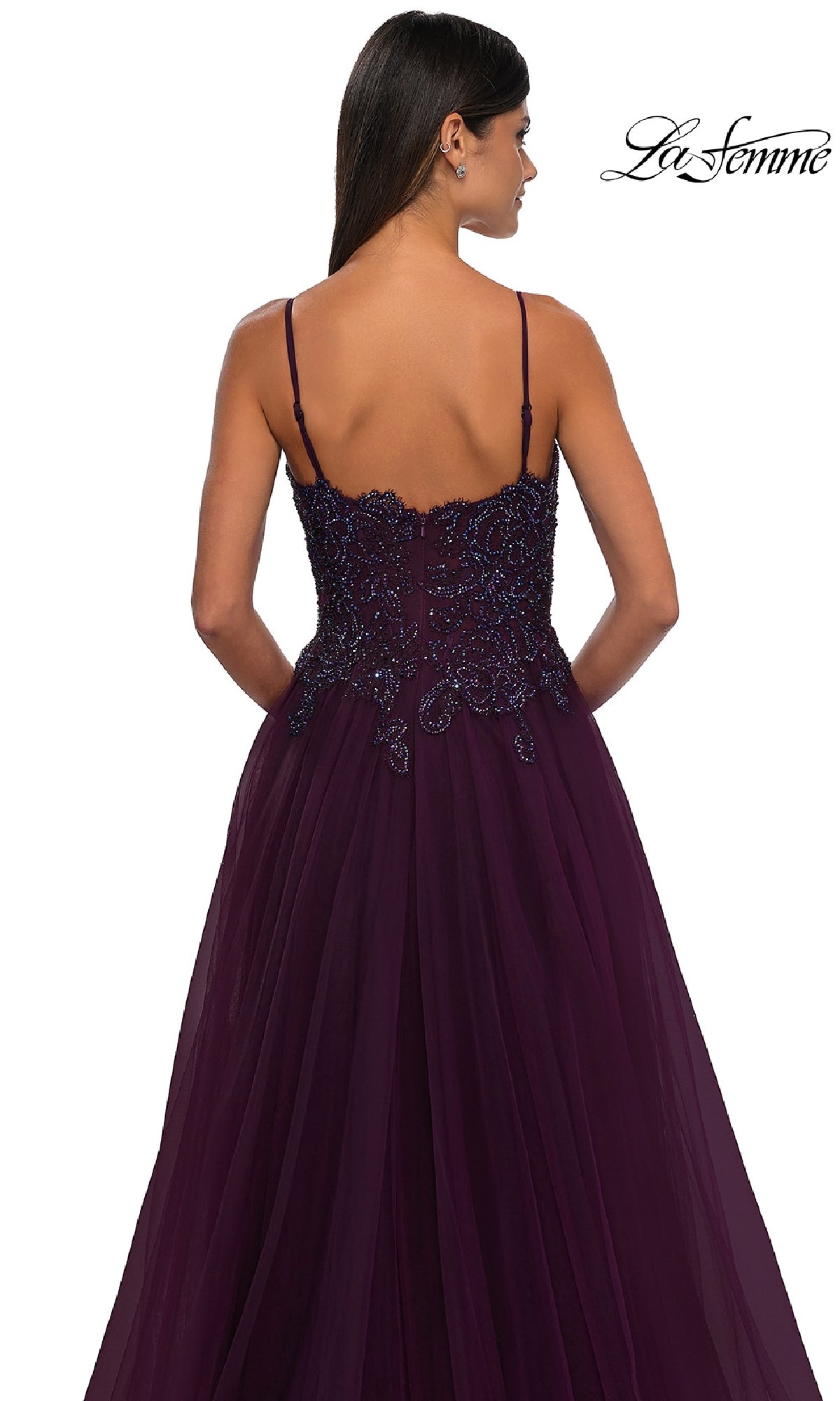Woman in a dark purple La Femme 32646 long prom ball gown with pockets, thin straps, and beaded details, shown from the back against a white background.