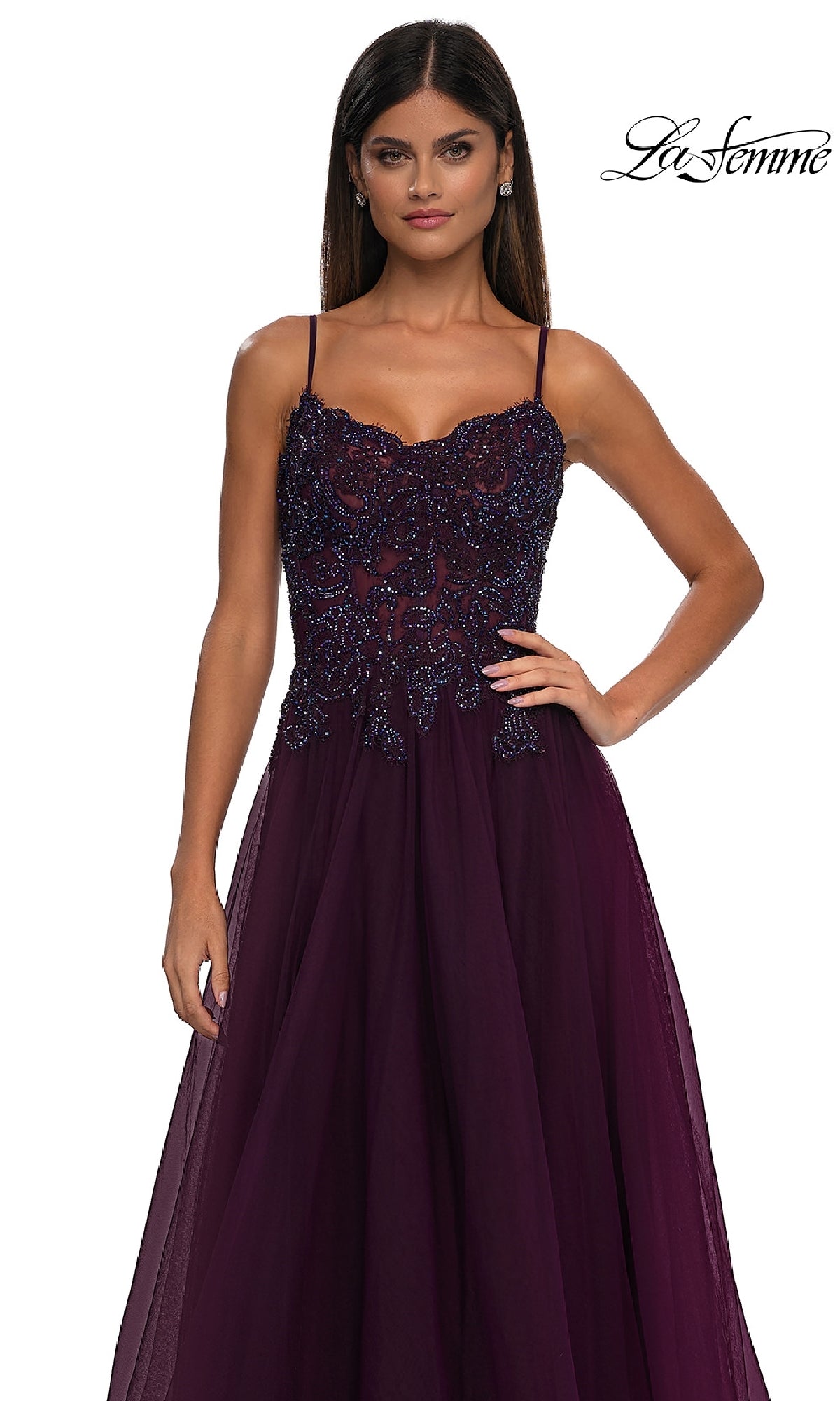 A woman wearing the Long Prom Ball Gown with Pockets: La Femme 32646, featuring thin straps and an intricately beaded bodice in deep purple, stands against a plain white background.