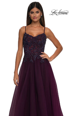 A woman wearing the Long Prom Ball Gown with Pockets: La Femme 32646, featuring thin straps and an intricately beaded bodice in deep purple, stands against a plain white background.