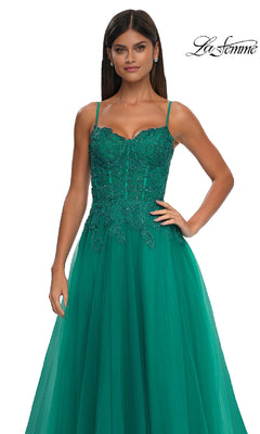 A woman poses with one hand on her hip in a sleeveless emerald green floral beaded gown with sheer overlay and pockets (La Femme 32646), against a white background. "La Femme" logo appears in the top right corner.