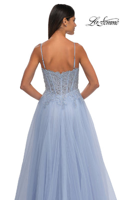 A woman faces away, wearing the La Femme 32646—a long blue prom ball gown with pockets, thin straps, lace details on a fitted bodice, and a flowing tulle A-line skirt.