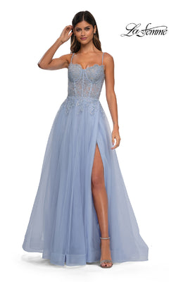 A woman models the La Femme 32646 Long Prom Ball Gown with pockets in light blue, featuring spaghetti straps, a sheer embellished bodice, and a high slit, standing against a white background.