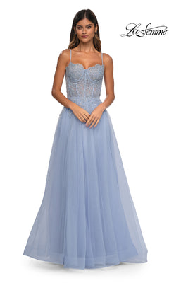 A woman in the La Femme 32646 long light blue lace and tulle A-line prom ball gown with thin straps and pockets stands against a white background. The La Femme logo is in the top right corner.