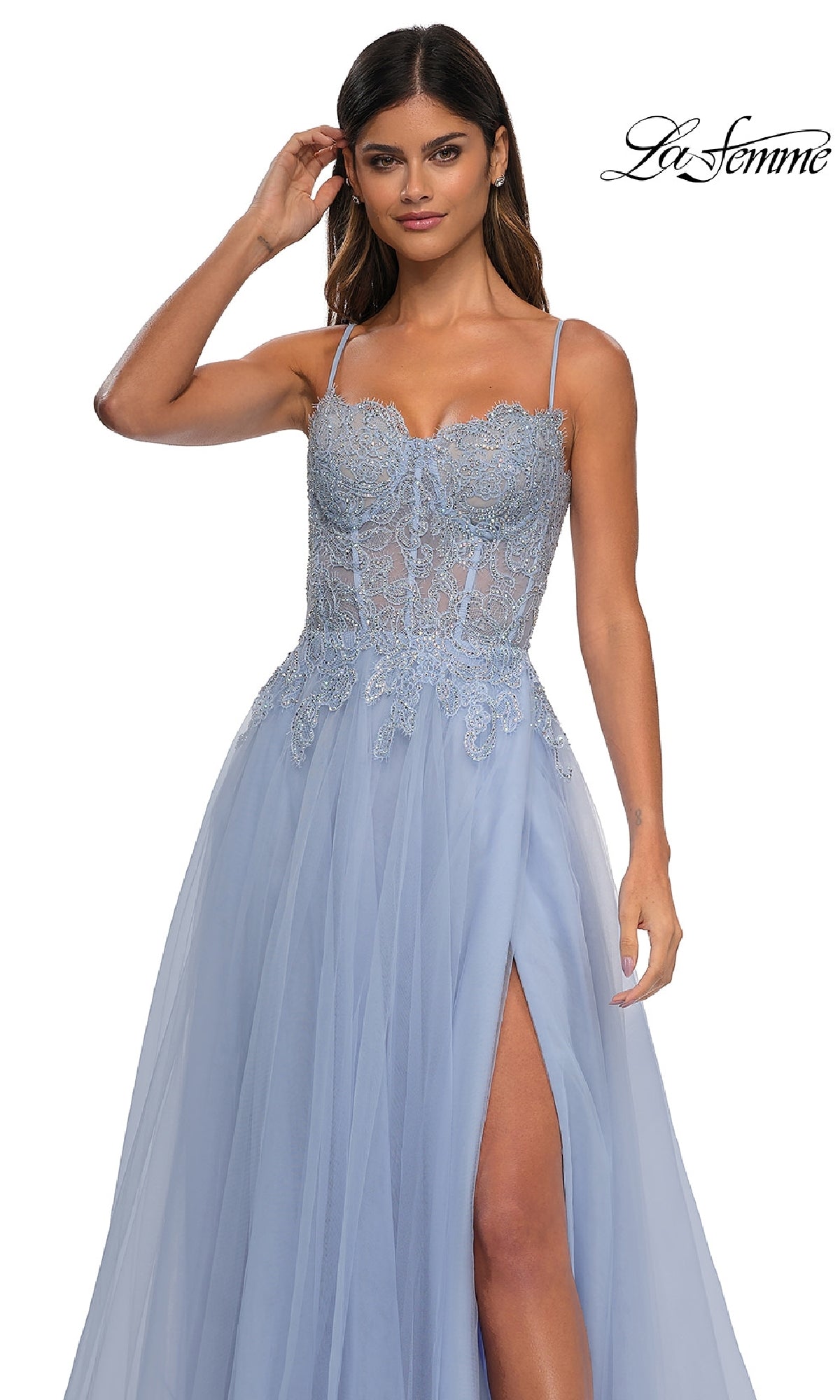 A woman stands against a white background wearing La Femme 32646, a long light blue prom ball gown featuring beaded floral lace embroidery, spaghetti straps, thigh-high slit, and pockets. The 