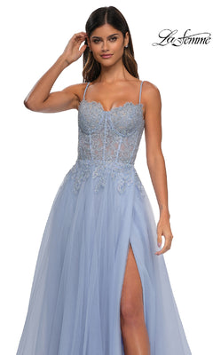 A woman stands against a white background wearing La Femme 32646, a long light blue prom ball gown featuring beaded floral lace embroidery, spaghetti straps, thigh-high slit, and pockets. The "La Femme" logo is in the top right corner.