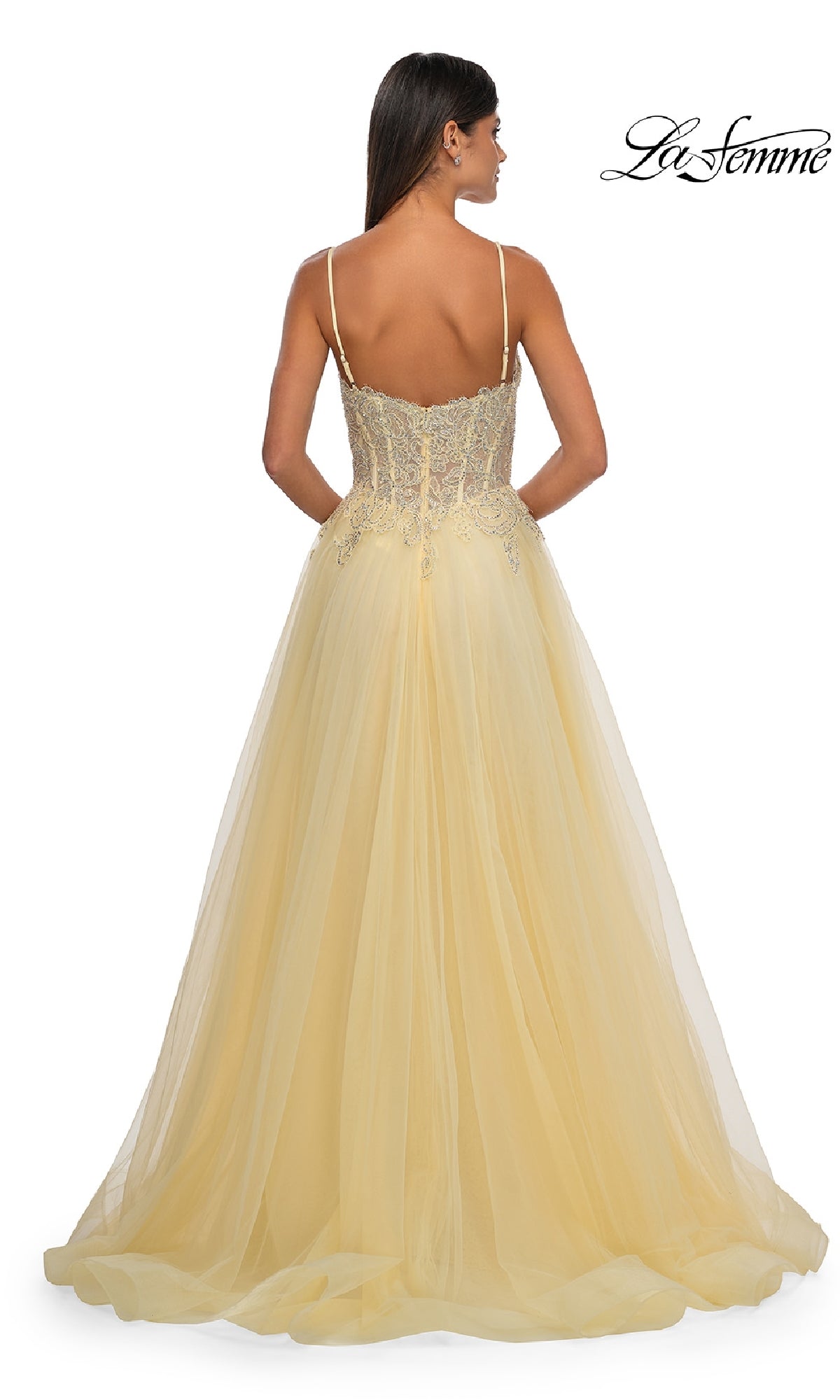 Woman in a yellow La Femme 32646 long prom ball gown with pockets, floor-length with thin straps and lace bodice detailing, shown from the back.