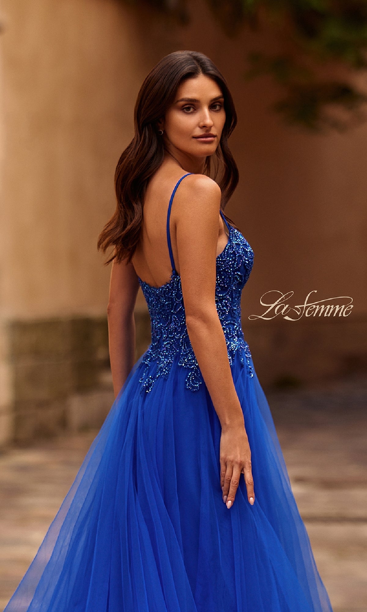 Woman in a sleeveless La Femme 32646 long prom ball gown with pockets stands outdoors, looking over her shoulder.