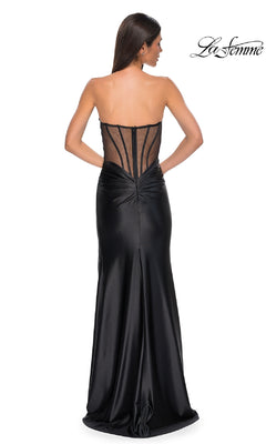 A woman poses with her back to the camera in the Sheer-Back Strapless Prom Gown La Femme 32649, featuring a sweetheart neckline, sheer corset-style back, and a flowing satin skirt.