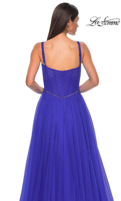 A woman faces away from the camera in a royal blue, floor-length La Femme 32956 prom gown featuring an a-line silhouette, beaded waist detail, and corset bodice, set against a white background with the "La Femme" logo in the top right corner.