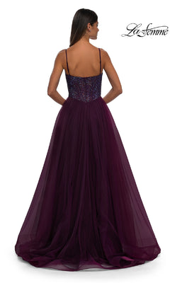 A woman faces away from the camera in a floor-length, dark purple La Femme 32668 prom ball gown with a beaded v-neck bodice, tulle skirt, and thin straps. The La Femme logo appears in the corner.