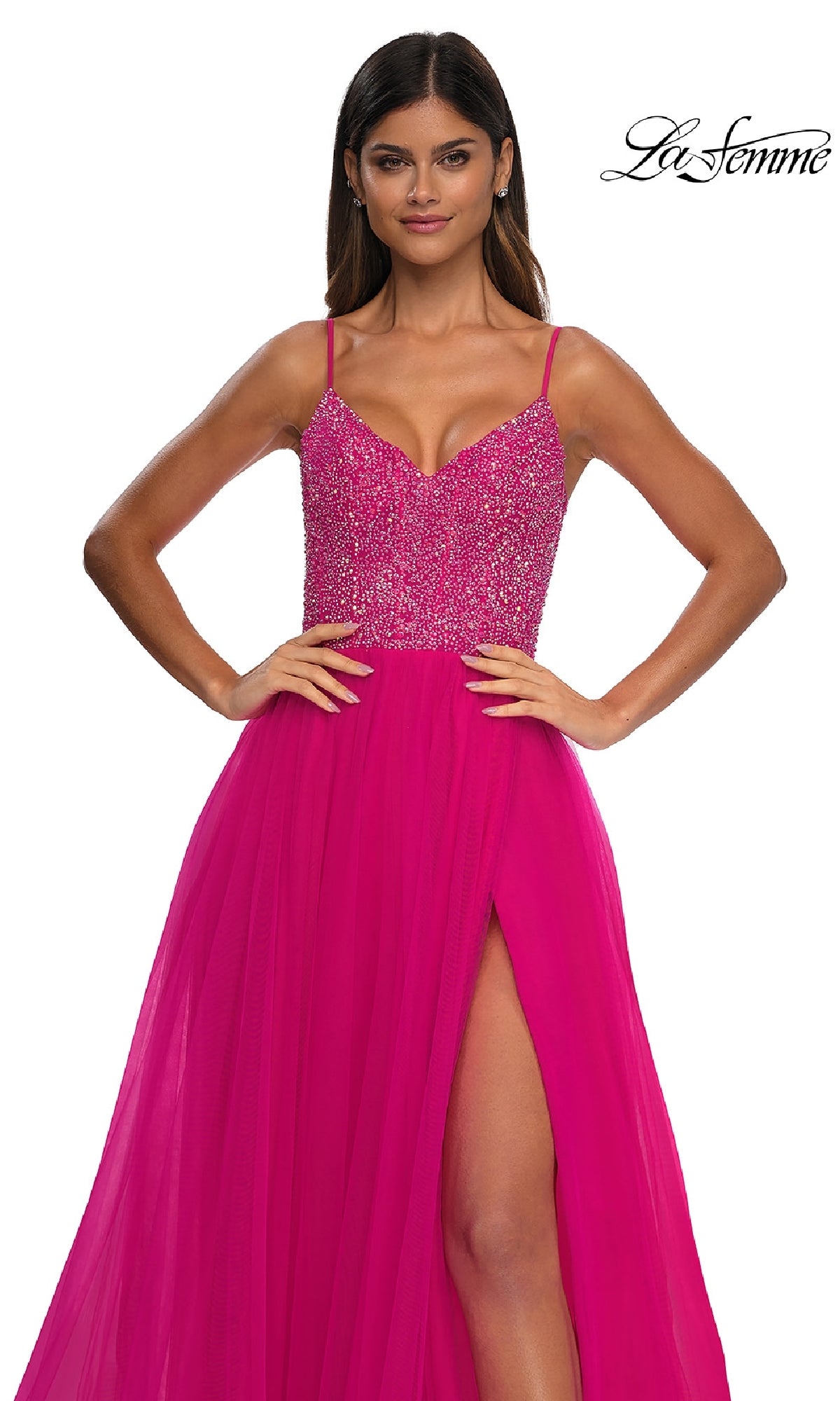 A woman stands with hands on hips in the Beaded-Bodice Long Prom Ball Gown (La Femme 32668), featuring a bright pink v-neck, beaded bodice, thin straps, and high slit against a white background. 