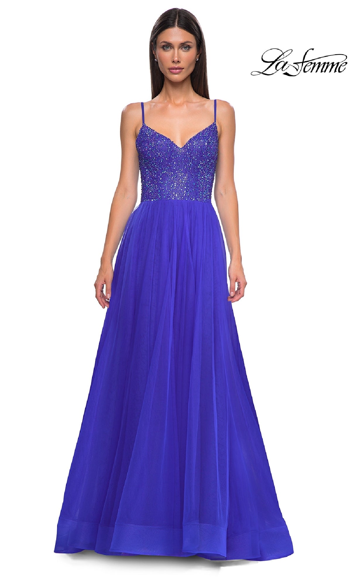 A woman wears the Beaded-Bodice Long Prom Ball Gown: La Femme 32668, a sleeveless royal blue a-line dress with a beaded v-neck bodice and tulle skirt, standing against a white background. The 