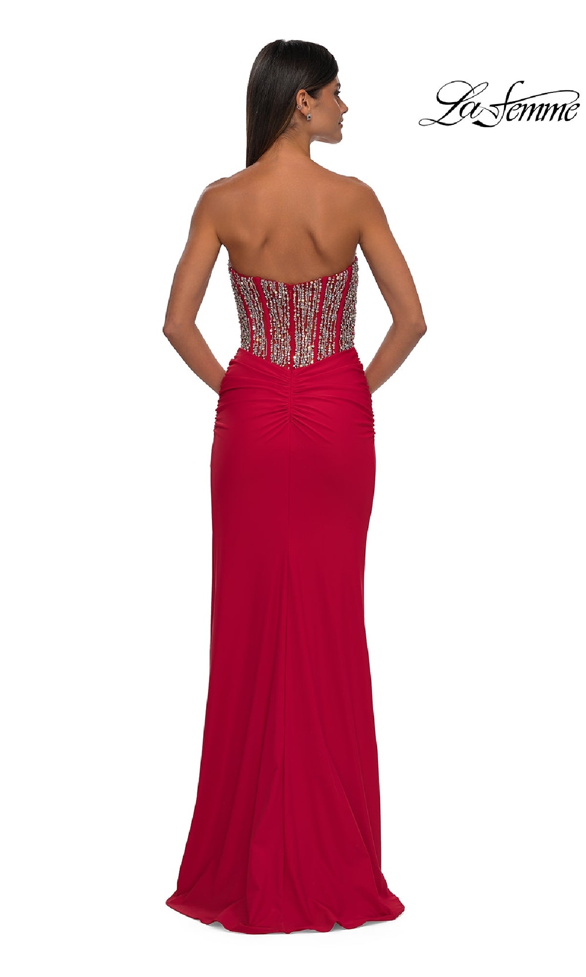 A woman poses with her back to the camera in the Strapless Long Corset Prom Dress: La Femme 32669, featuring a beaded corset bodice and ruched detailing. 
