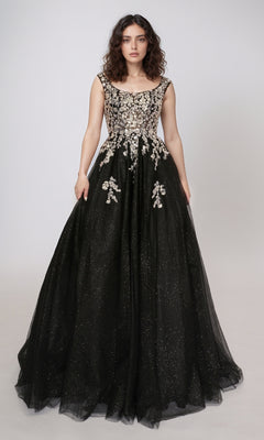 A woman in the Nina Canacci 3266 long prom dress—black glitter tulle with a fitted, embellished bodice and floral appliqués—stands against a plain light background.