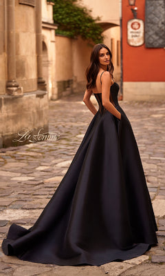 A woman in a Sheer-Corset Long A-Line Prom Gown: La Femme 32670 stands on a cobblestone street, looking over her shoulder.