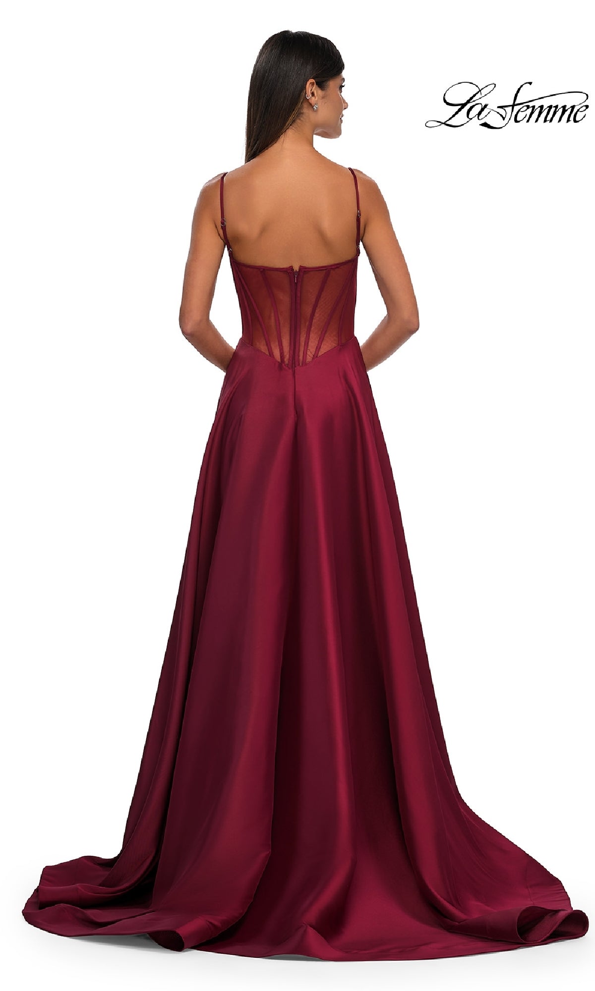 A woman stands facing away in the Sheer-Corset Long A-Line Prom Gown, La Femme 32670—a floor-length, burgundy Mikado dress with spaghetti straps, a fitted bodice, sheer-back detail, and a flowing skirt.