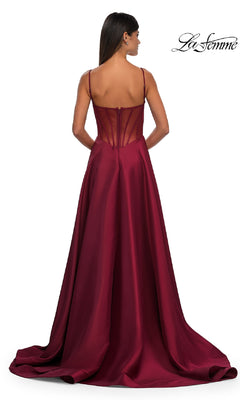 A woman stands facing away in the Sheer-Corset Long A-Line Prom Gown, La Femme 32670—a floor-length, burgundy Mikado dress with spaghetti straps, a fitted bodice, sheer-back detail, and a flowing skirt.